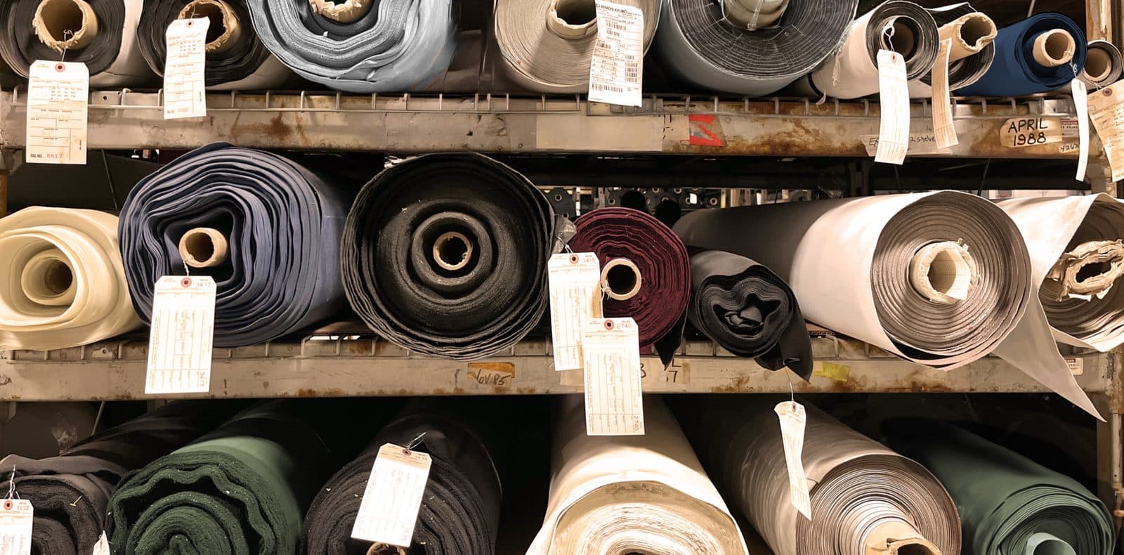 Paper-tagged surplus rolls on warehouse racking at Core Products Group — handwritten inventory tags, automotive and contract-grade material