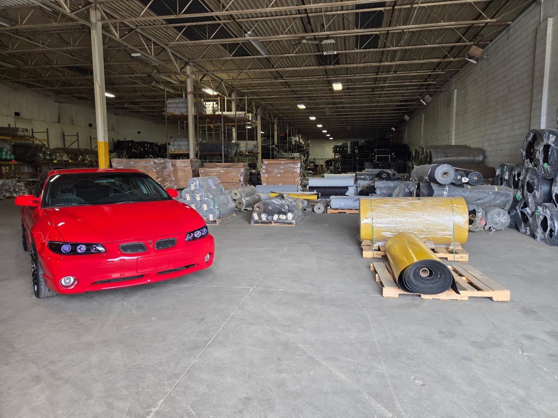 Core Products Group surplus warehouse in Livonia, MI — palletized rolls, drums, wrapped goods and reclaimed inventory across the floor